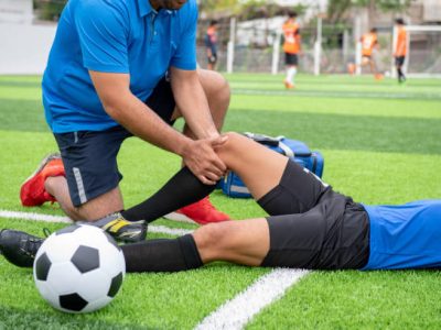 low section of male physical therapist rubbing soccer player knee on field